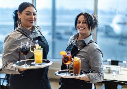 Two friendly servers with trays holding cocktails