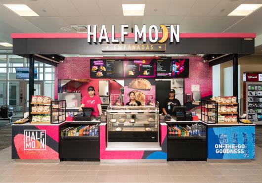 Store front photo of Half Moon Empanadas with bright colors and employees ready to serve customers.
