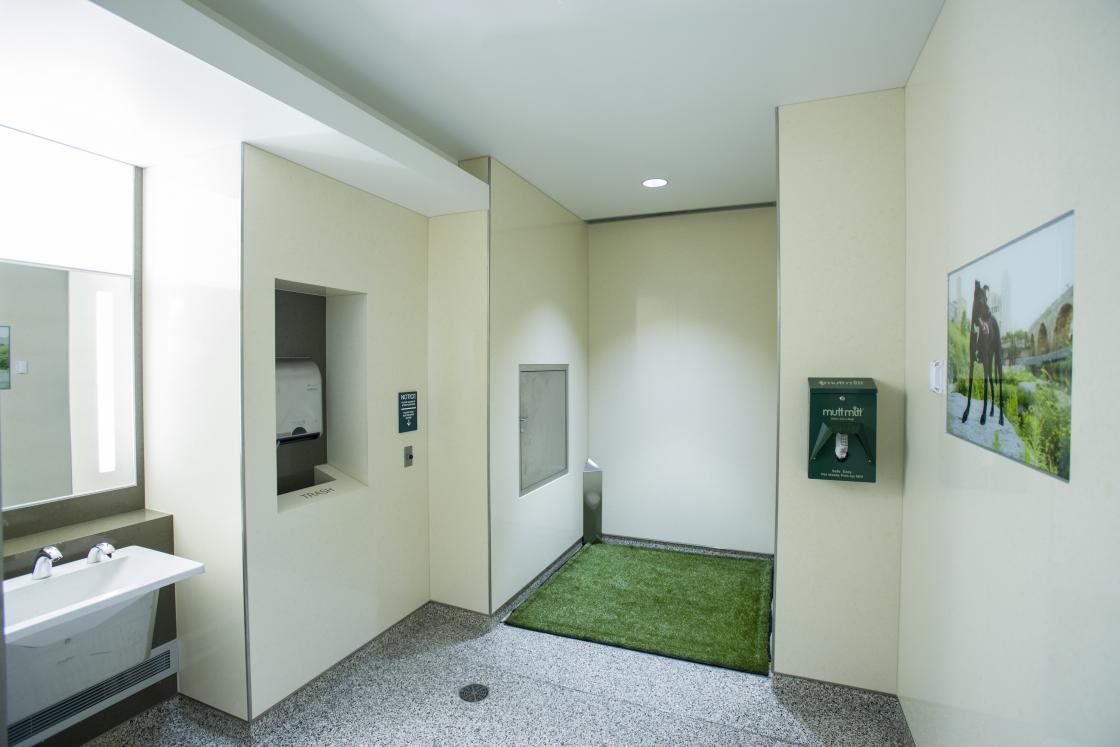 Interior view of an indoor animal relief area featuring a grassy area, sink and complimentary waste bags