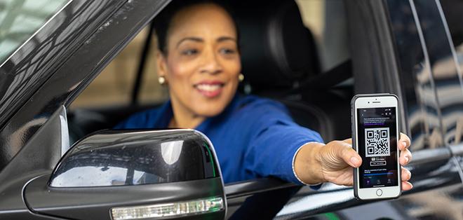 A woman holding her phone with a QR code up to the machine at the parking entrance. 